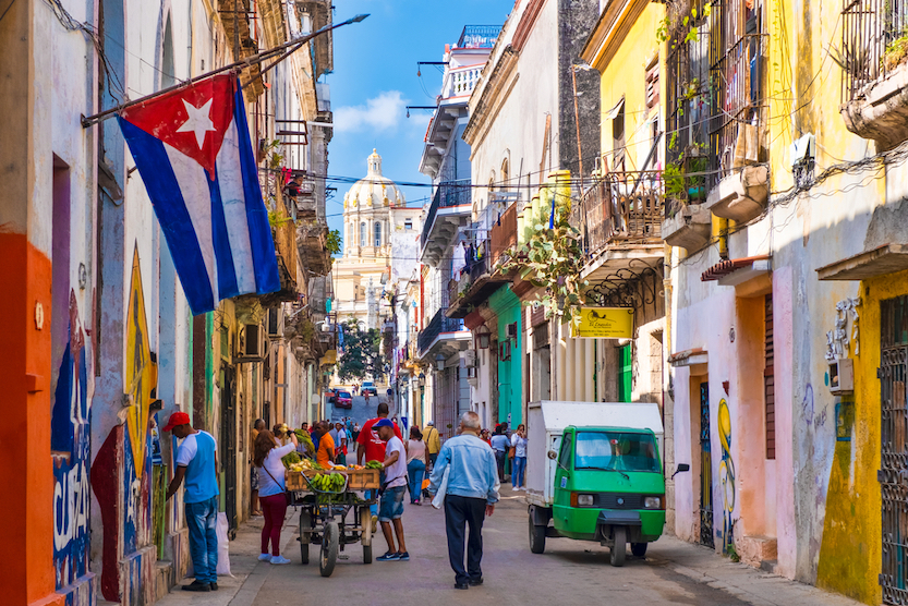Best countries to visit in August, Street scene with cuban flag on a colorful street in Old Havana - Best countries to visit in August, Street scene with cuban flag on a colorful street in Old Havana