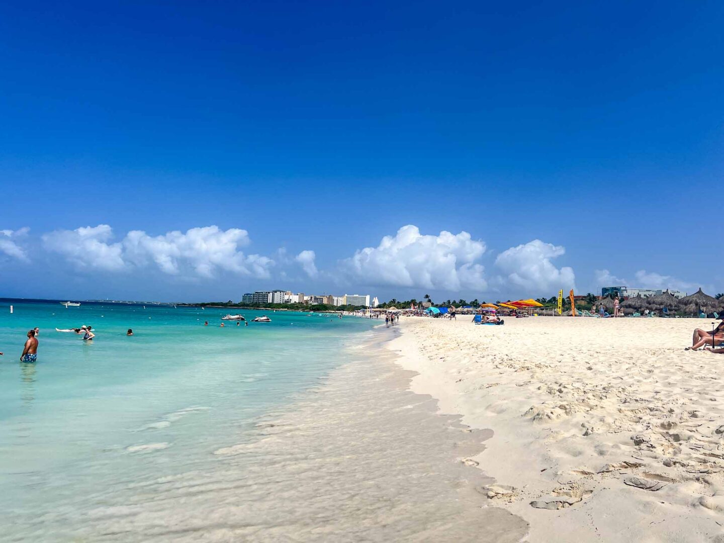 Best countries to visit in August, beach with white sand and blue water and sky in Aruba - Best countries to visit in August, beach with white sand and blue water and sky in Aruba